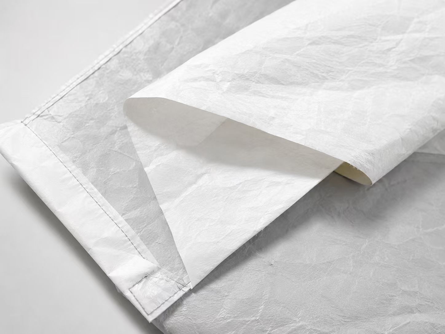 Lightweight paper-like nonwoven material with flexible protective fabric structure